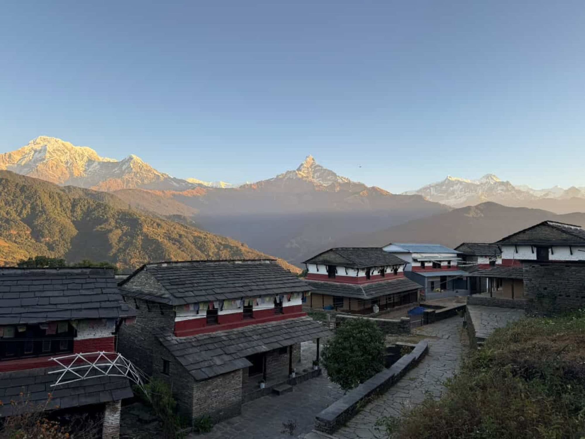 First light striking the Annapurna peaks above the slate roofs of a hillside village.